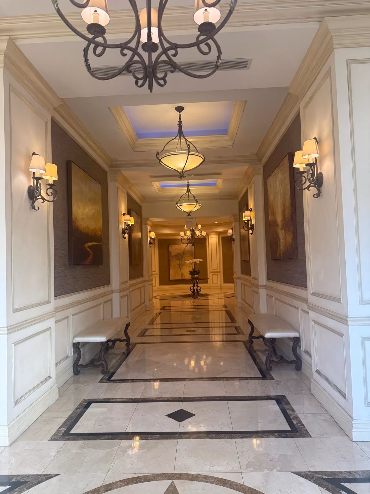The marble corridor leading to Mimi's Touch Salon, lit by wall sconces and chandeliers.